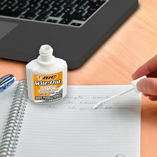 Open correction fluid bottle with brush applying on notebook.